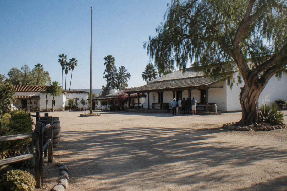 The open plaza of Old Town San Diego State Historic Park, with low adobe buildings, wooden verandas and a pepper tree.