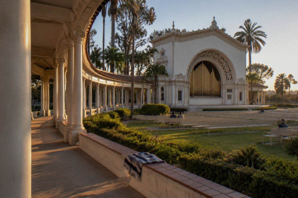 An ornate open air organ pavilion with gardens and tall trees in a city park