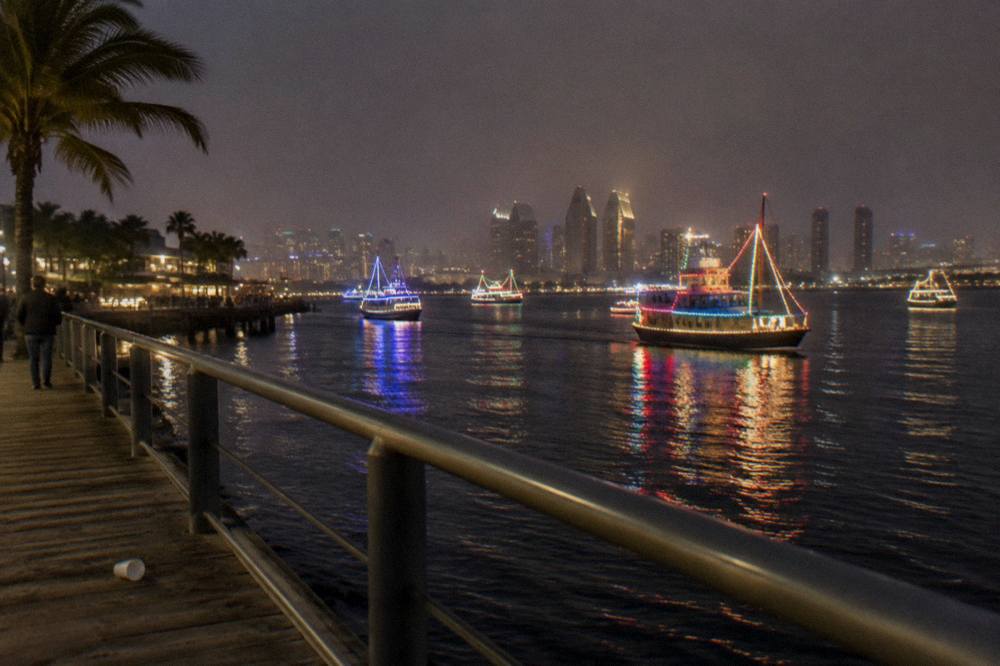 Boats strung with lights crossing a dark bay at night with the city skyline behind them
