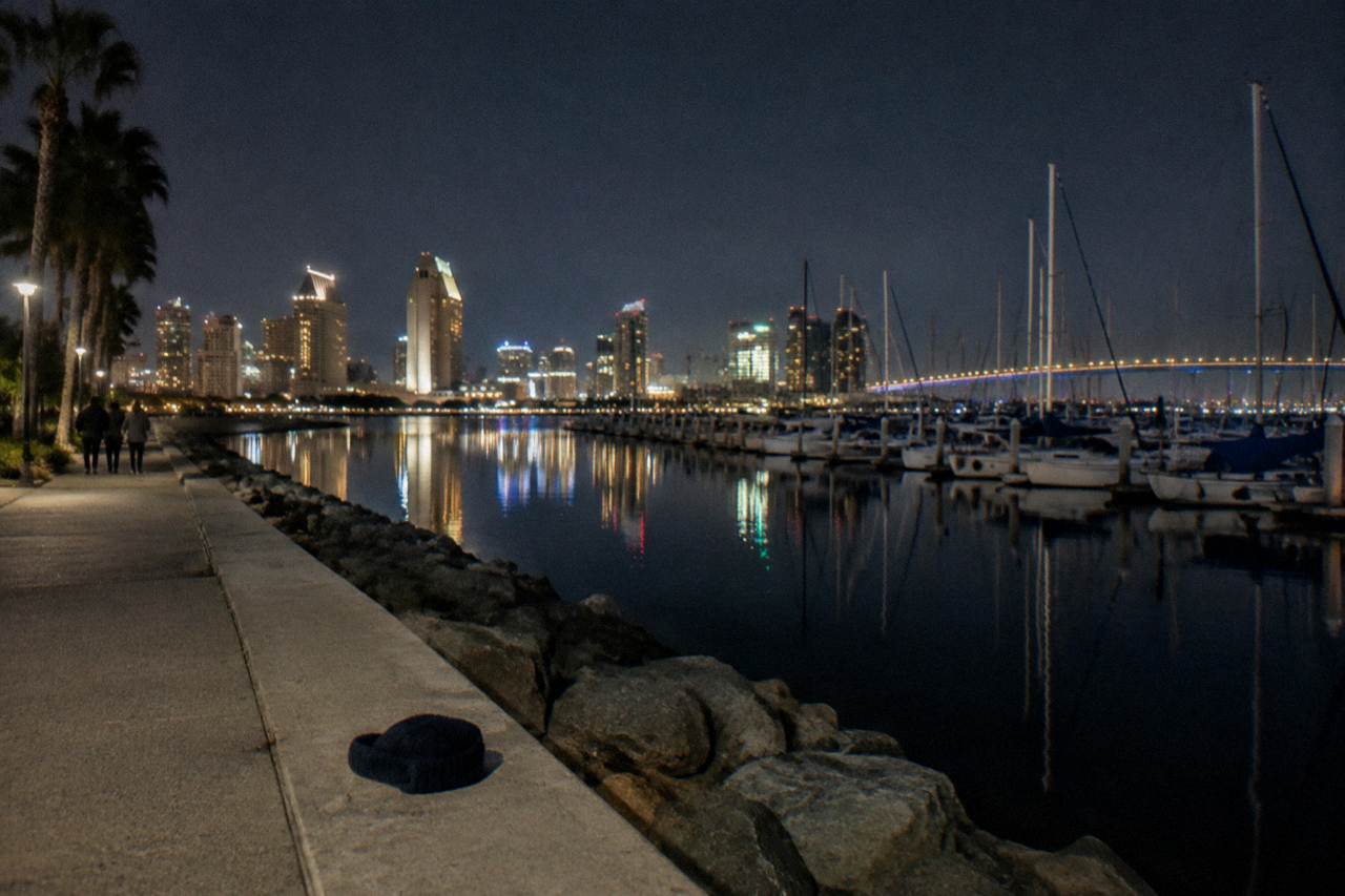 A dark bay at night with boat lights and the city skyline reflected on the water