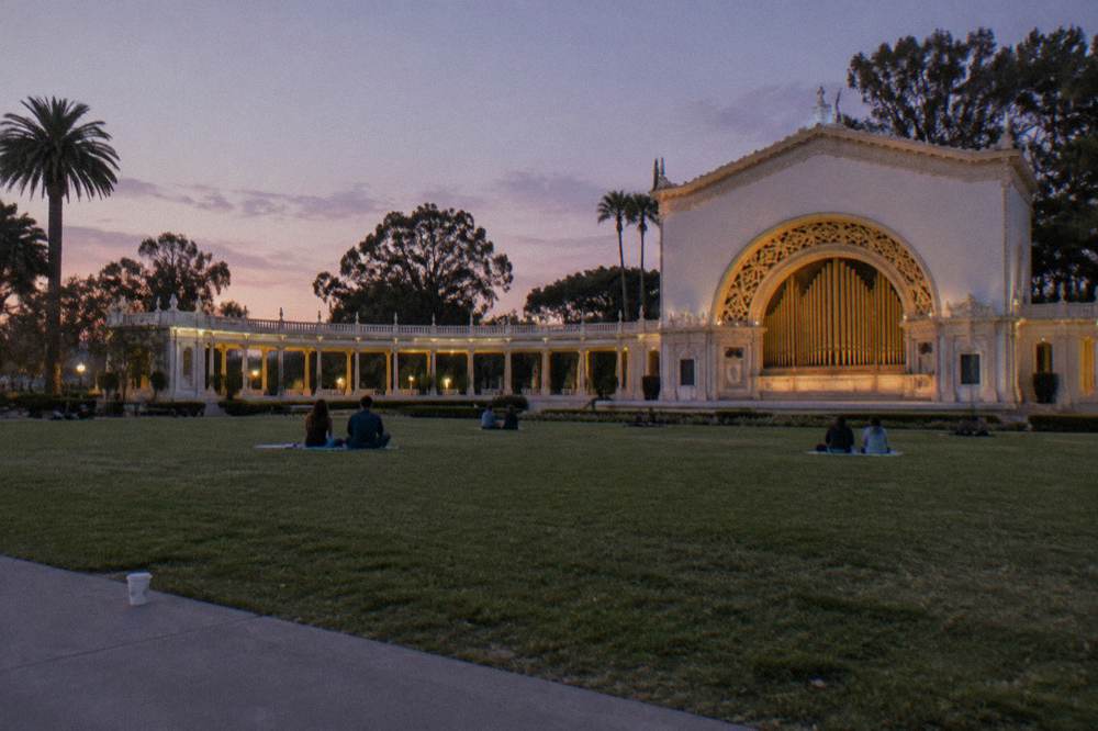 An outdoor pipe organ pavilion with tall colonnades facing a broad open lawn under an evening sky.