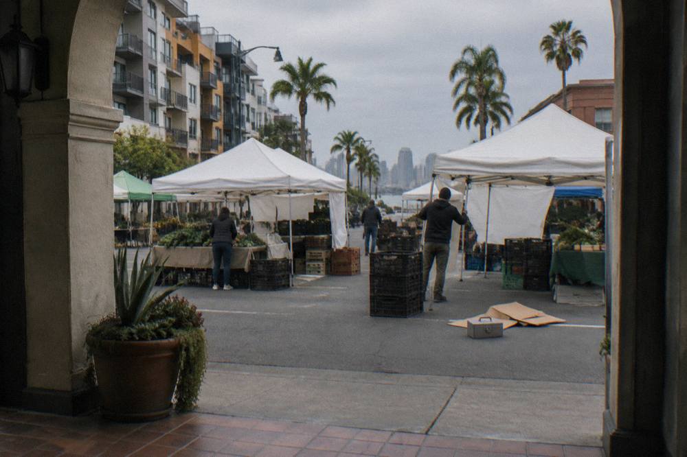 Farmers market stalls with crates of produce and canvas awnings along a city street