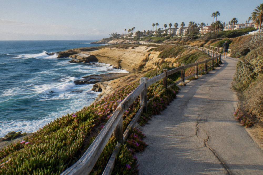 A paved coastal path along a bluff above breaking blue waves
