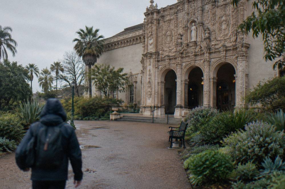 A museum entrance portico with arched doorways along a garden walkway in Balboa Park