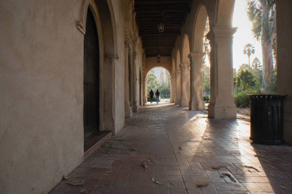 A shaded walkway in Balboa Park lined with trees and Spanish-style building facades