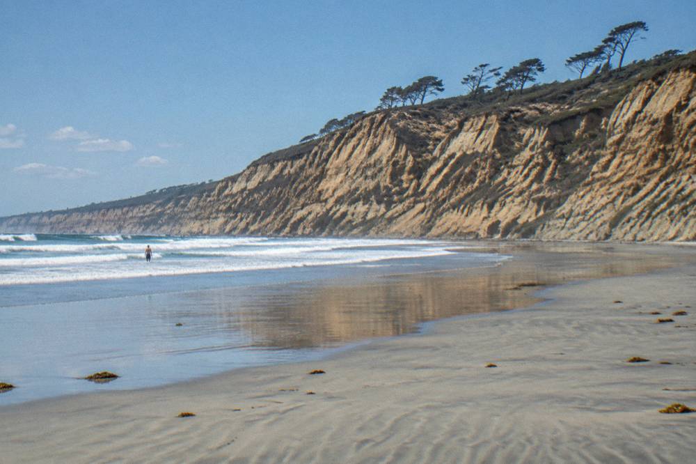A wide sandy beach below tall cliffs with waves rolling in
