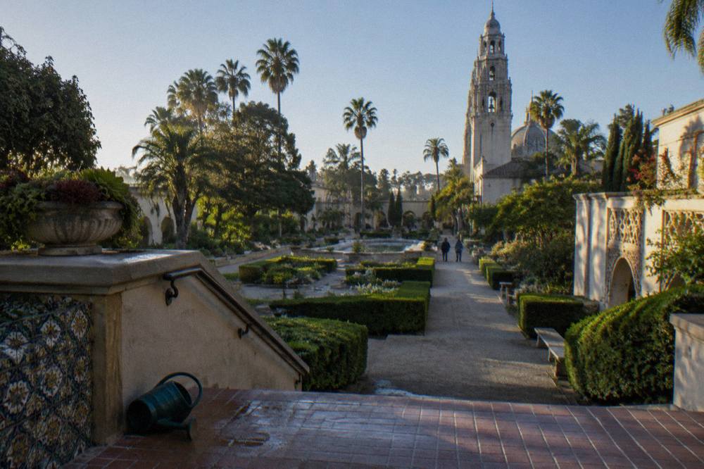 Gardens and museum building facades along a Balboa Park walkway in morning light