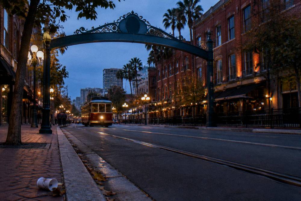 A downtown street with an ornate arch sign and trolley tracks in evening light
