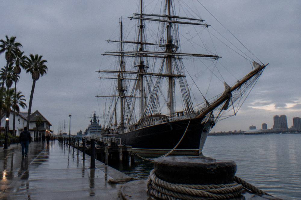Historic sailing ship masts along a waterfront promenade at dusk