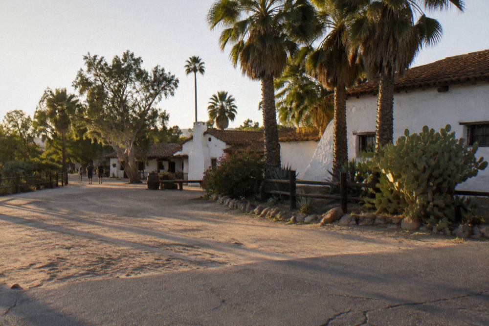 Open parking lot beside Old Town San Diego adobe buildings and palm trees