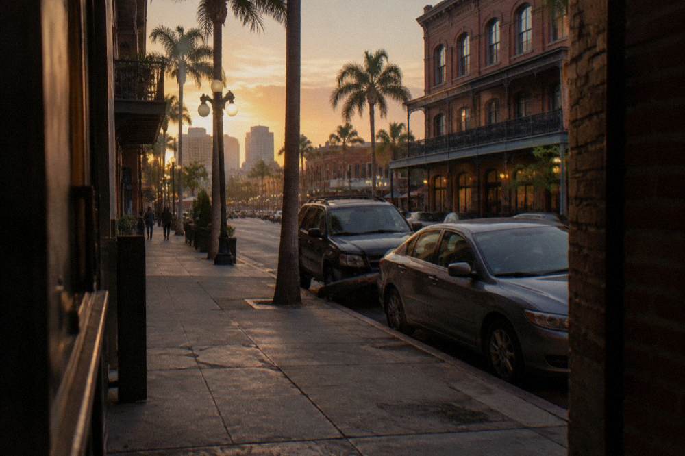 Downtown San Diego sidewalk with historic building facades and cars parked along the curb
