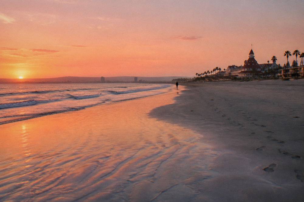 Open sand at sunset with soft light over calm water and a long empty shoreline