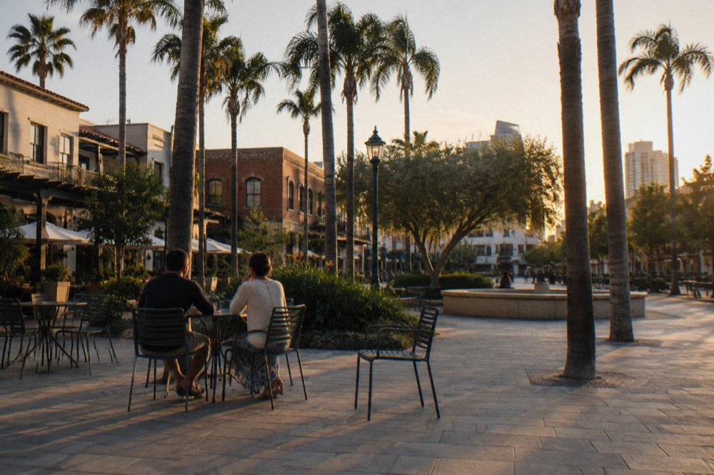 An open public square with trees and cafe tables in warm evening light