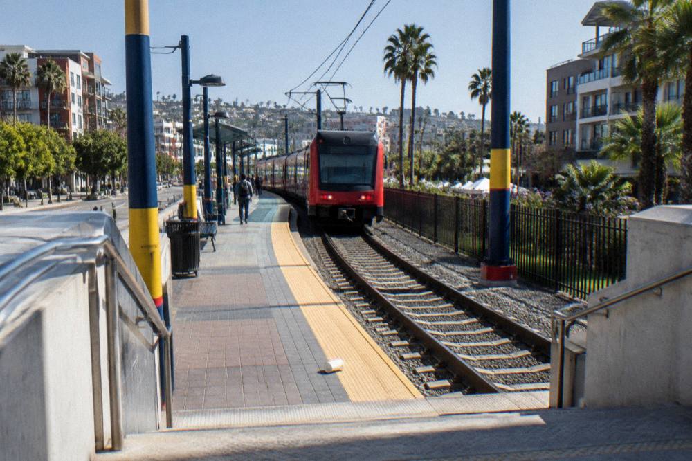 A transit station platform with a route sign and tracks under a clear sky