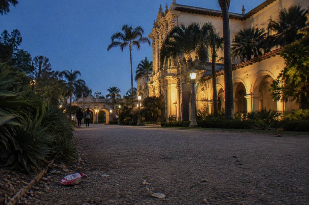Balboa Park's lit building facades and gardens seen along an empty walkway in the evening
